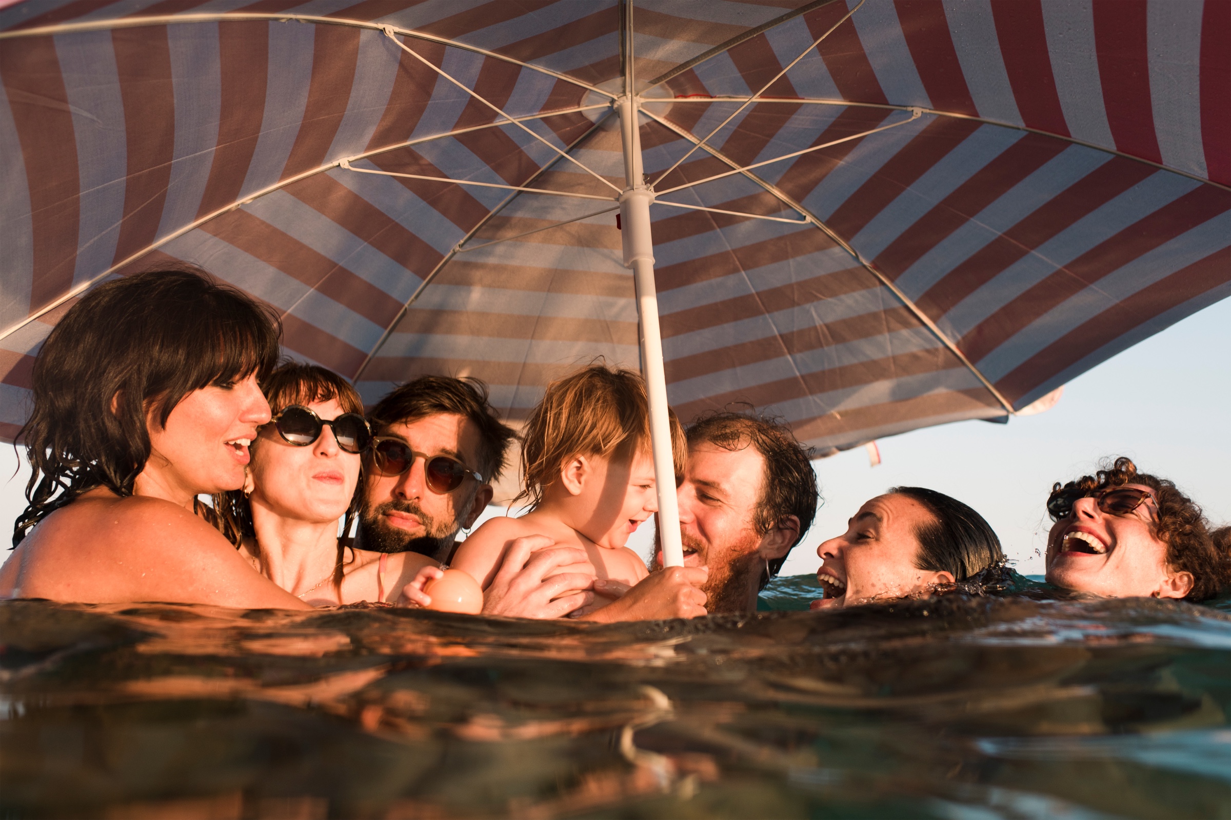 Friends and family laughing together in the water under a beach umbrella