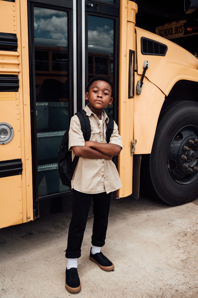 Child standing with arms crossed in front of a school bus